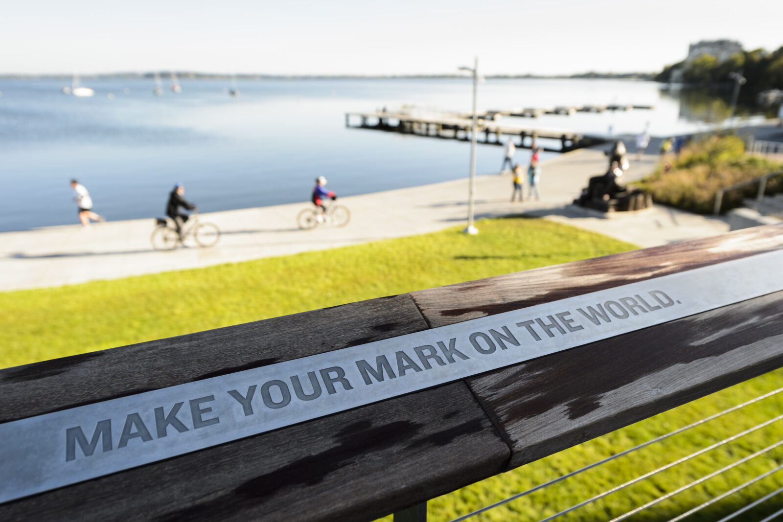 Make your Mark on the world inscribed on a rail with lake Monona nearby.