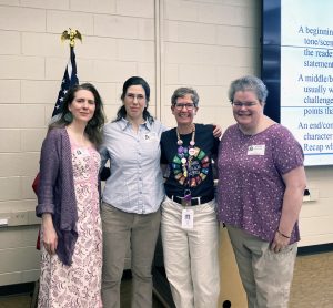 Four staff members stand near presentation screen